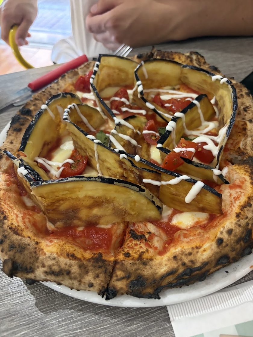 A pizza fanned with long slices of roast aubergine over tomato and mozzarella, with cherry tomatoes and a cream drizzle, on a heavily blistered crust