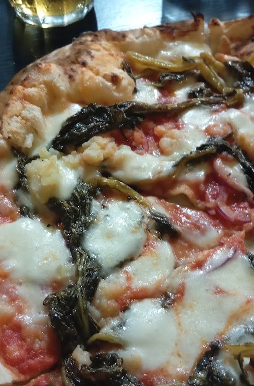 A close, tall crop of a pizza topped with dark braised greens and melted mozzarella over tomato