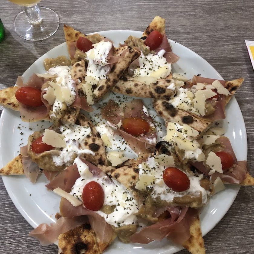 Wedges of pizza crust arranged on a white plate with Parma ham, stracciatella, cherry tomatoes, parmesan shavings and black pepper